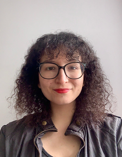 A portrait of Eylul Oguz looking at the screen with glasses and brown curly hair